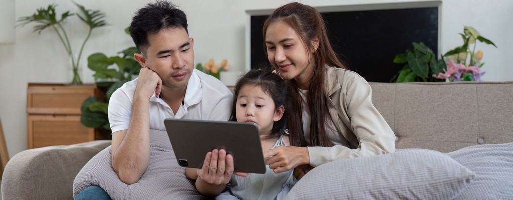 Des parents et leur enfant regardent la tablette dans le canapé