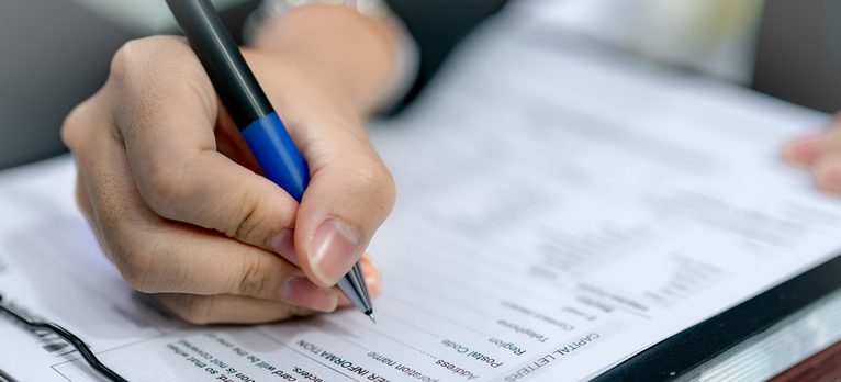 une main teint un stylo et remplis une fiche d'inscription